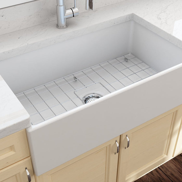 White fireclay apron-front farmhouse kitchen sink installed in a bright kitchen with marble countertops