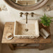 Stone sink on a wooden vanity with a mirror above, in a rustic bathroom setting. Troia Light Rustic Travertine Rectangular Above Vanity Bathroom Sink Hand Chiseled Exterior