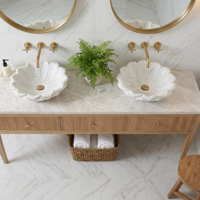 Bathroom vanity with two white sinks, gold fixtures, and a plant on a marble floor.