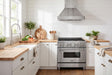 ZLINE 36-inch stainless kitchen set staged together in a farmhouse kitchen: RA36 gas range, 655-4SSSS-36 wall hood mounted above, and Apollo brushed-nickel faucet at the sink